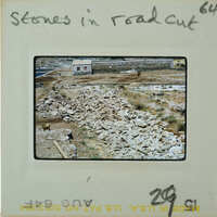 Pile of rocks on dirt ground with a building in the background.