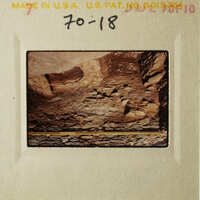 This is an old photograph depicting a rocky landscape with a small structure, possibly a cave entrance, and some debris on the ground.