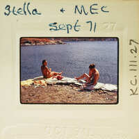 Two people sitting on a rock near water with a handwritten note and date on the photo. Catalog number KC.111.27