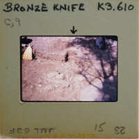 A photograph of a bronze knife on display with an explanatory label and a shadowed background.