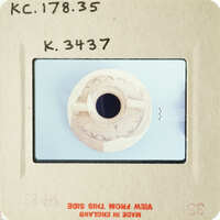 A small, intricately carved wooden object with a hole in its center.