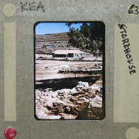 A vintage photo of a stone house with trees and mountains in the background.
