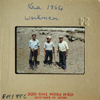 Three men standing on dirt ground, possibly at work site.