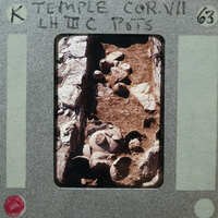 Stone wall on left with pottery on ground in center.