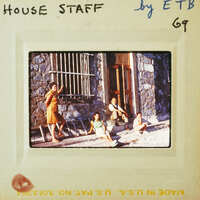 A vintage photograph of a group of people sitting outside a building with barred windows.