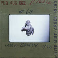 A small, dark-colored figurine on a white surface with a label and handwritten notes.