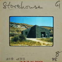 Old stone building with people standing outside, set against a mountainous landscape.