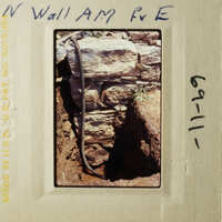 A photograph depicting an old brick wall with a metal pipe running through it, taken from a low angle.