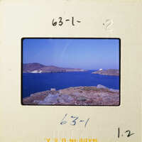 A photograph showing a scenic view of a coastline with mountains and water under a blue sky.