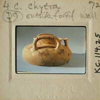 Ancient clay pot with handle and spout, displayed on light gray surface.