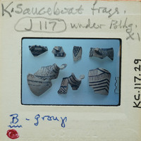 A collection of ancient Greek pottery shards on a white surface with labels and notes.