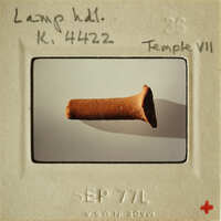 Brown clay artifact on white surface with shadow, labeled as "Lamp Handle" from Temple VII.