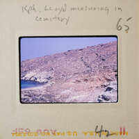 A photograph of a rocky coastline with a body of water and a hilly landscape.