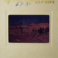 This is an image of a vintage photograph depicting a barren landscape with a few scattered objects, possibly taken from a car window, as indicated by the reflection and the angle of the shot.