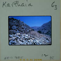 Old photograph of a stone wall with mountains and blue sky in the background, labeled "Karthaia".