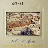 The photograph shows an ancient stone structure, possibly ruins, with layers of brick and stone, taken from a distance.