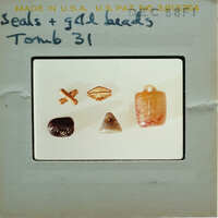 A collection of small objects, including beads and stones, displayed on a white surface with labels indicating they are from "Tomb 31".