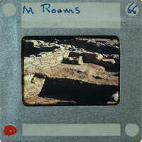 A photograph of an archaeological site with ruins and excavated areas, presented on a vintage film strip card.