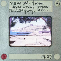 A vintage photograph of a coastal town with a clear blue sky and sea, framed by trees.