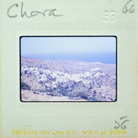 A vintage photograph of a coastal village with blue water and mountains, labeled "Chora" on the border.