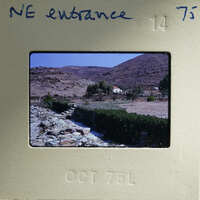 Old photograph of a rural landscape with mountains, trees, and a stone wall.