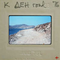 A photograph of a dirt road leading to the ocean with mountains in the background, dated August 1976.