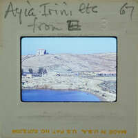 A photograph of a coastal landscape with a body of water, hills, and buildings.