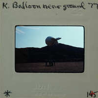 A large balloon on the ground with people standing around it.