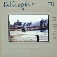 Helicopter parked on a dirt area with mountains in the background.