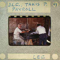 Two men working at a table with papers, possibly reviewing documents or conducting an inspection.