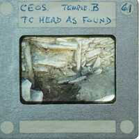 Terracotta figurine face next to stone wall.