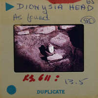 Terracotta figurine head on surface with walls.