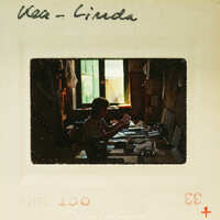 Black and white photograph of a person sitting at a desk with papers, labeled "Kea - Linda" on the border.