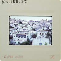 A vintage photo of a coastal town with white buildings and blue roofs, printed on an old-fashioned film strip.