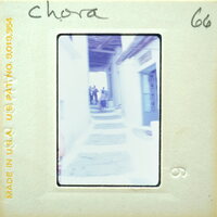 A vintage photograph of a narrow alleyway with buildings on either side and people walking.