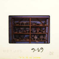 Old photograph with shelves displaying various vases and pottery.