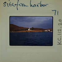 This is a photograph of a harbor with boats and houses on an island, taken from the water's edge.