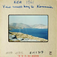 View across bay to mountains with blue water and rocky shore.