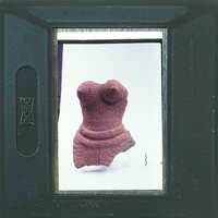 A small, ancient clay figurine displayed on a white background with a camera viewfinder framing the image.