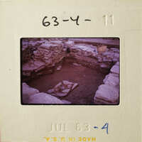 Old photograph of an archaeological site with stone ruins and a pit.