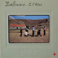 A vintage photo of a balloon crew on a rocky hillside with a blue sky background.