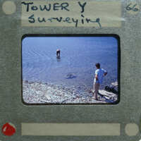Image of a person standing on the shore while another person is wading into water, with a vintage film strip border and title "TOWER SURVEYING".