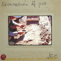 A person working on a construction site, digging through dirt and debris with a shovel.