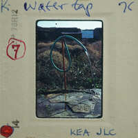 A photograph of a garden hose coiled on a metal stand, with water dripping from it onto stone tiles.