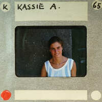 A young woman with a smile on her face, wearing a striped top and standing against a wall.