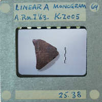 A small, dark triangular object with markings on a white surface, photographed and labeled as an artifact from the A.R.M.I. collection.