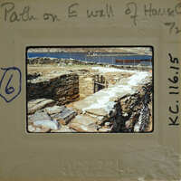 Old photograph of a stone wall with a path leading to it, possibly from an archaeological site.