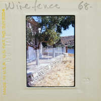 A photograph of a wire fence with trees and mountains in the background, taken during daylight.