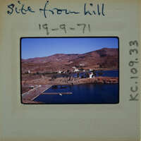 A vintage photo of a scenic coastal landscape with mountains, water, and buildings.