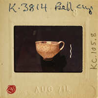 A photograph of an antique cup on a white card with handwritten details and a red stamp at the bottom.